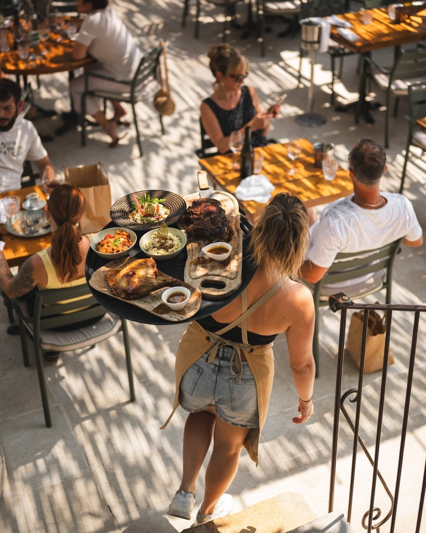 En plein service : un plateau de viandes et de planches porté en terrasse, entre les tables au soleil